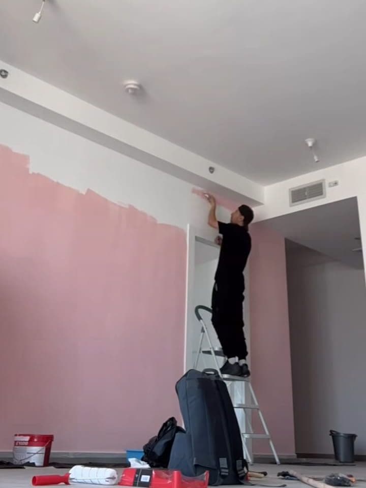 Painter on a stepladder cutting in pink paint along the ceiling line