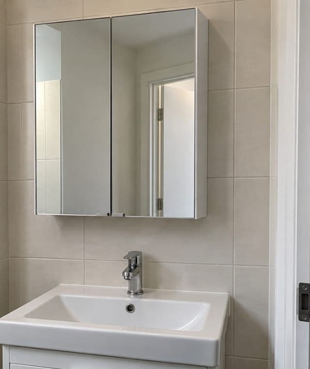 Mirrored cabinet mounted on a tiled wall above a bathroom basin