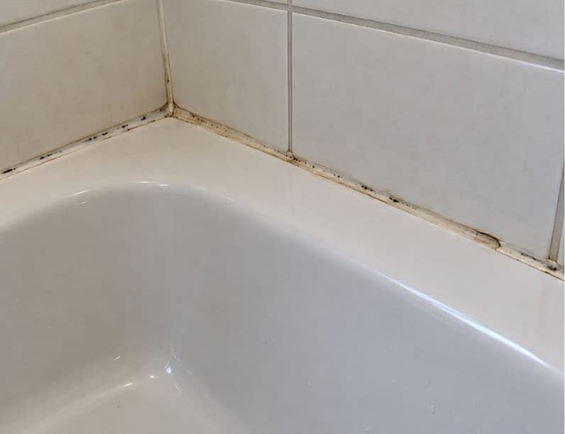 Old, mould-stained silicone along the edge of a bath