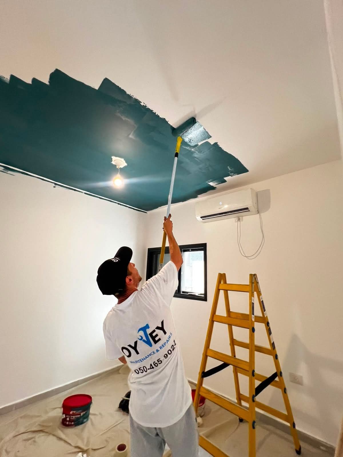 Oy Vey team member rolling deep teal paint onto a ceiling, wearing an Oy Vey T-shirt