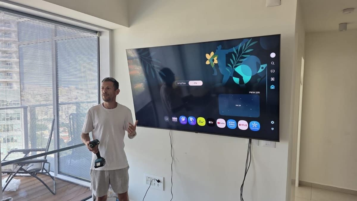 Large TV mounted on a living-room wall, with the installer beside it